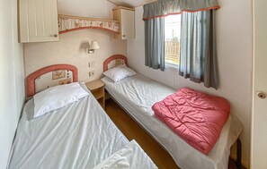 A room with two single beds, a small table, a wall-mounted lamp, and a window with curtains.