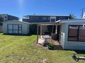 A residential property with a covered patio, a small garden, and a neighboring house. - Hosts on the Coast Ocean Corner (Whangamata)