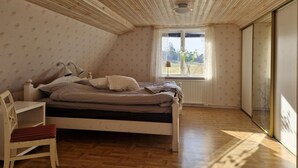 Een slaapkamer met een bed, een stoel, een raam met uitzicht en houten vloeren.
