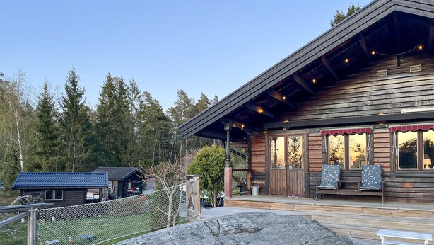 A wooden lodge with a covered porch, a fenced outdoor area, and a view of the surrounding forest. - Beautiful home in Strängnäs with sauna (Strängnäs)