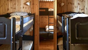 Une petite pièce avec des lits superposés, des murs en bois et deux lampes de chevet.