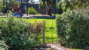 A playground with a swing set and slides, surrounded by greenery and a fence. - Perfect 3-bed Higgins Surf Shack@the park by the Point in enchanting Middleton (Middleton)