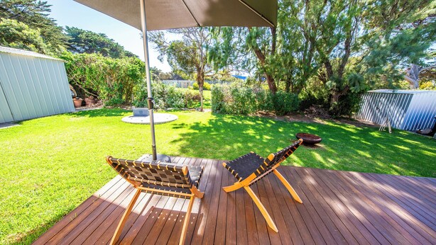 A wooden deck with two lounge chairs and a table, surrounded by a well-maintained lawn and trees. - Perfect 3-bed Higgins Surf Shack@the park by the Point in enchanting Middleton (Middleton)