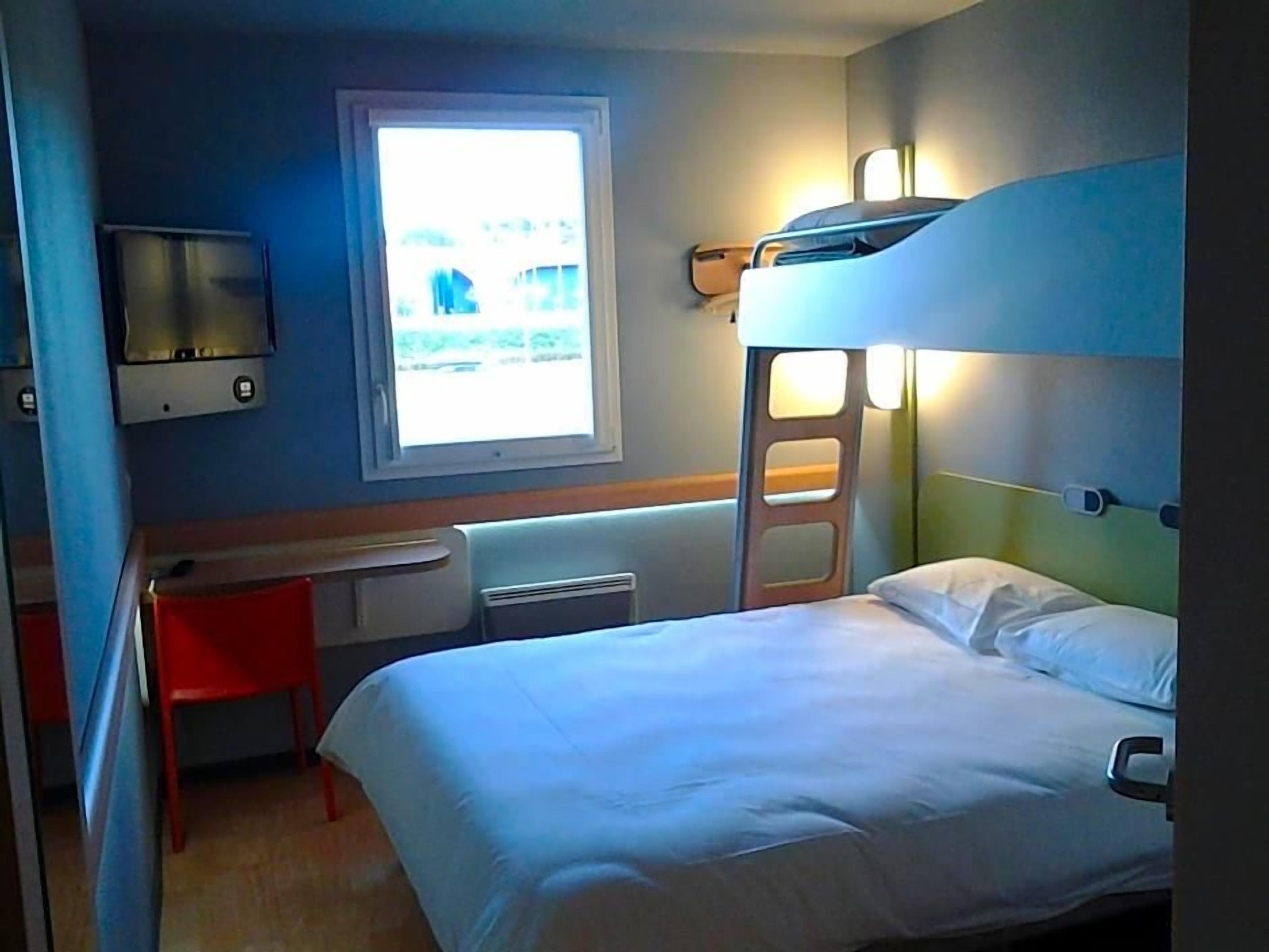 Een slaapkamer met stapelbed, bureau en stoel, een raam en een tv aan de muur.