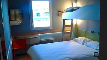 Een slaapkamer met stapelbed, bureau en stoel, een raam en een tv aan de muur.