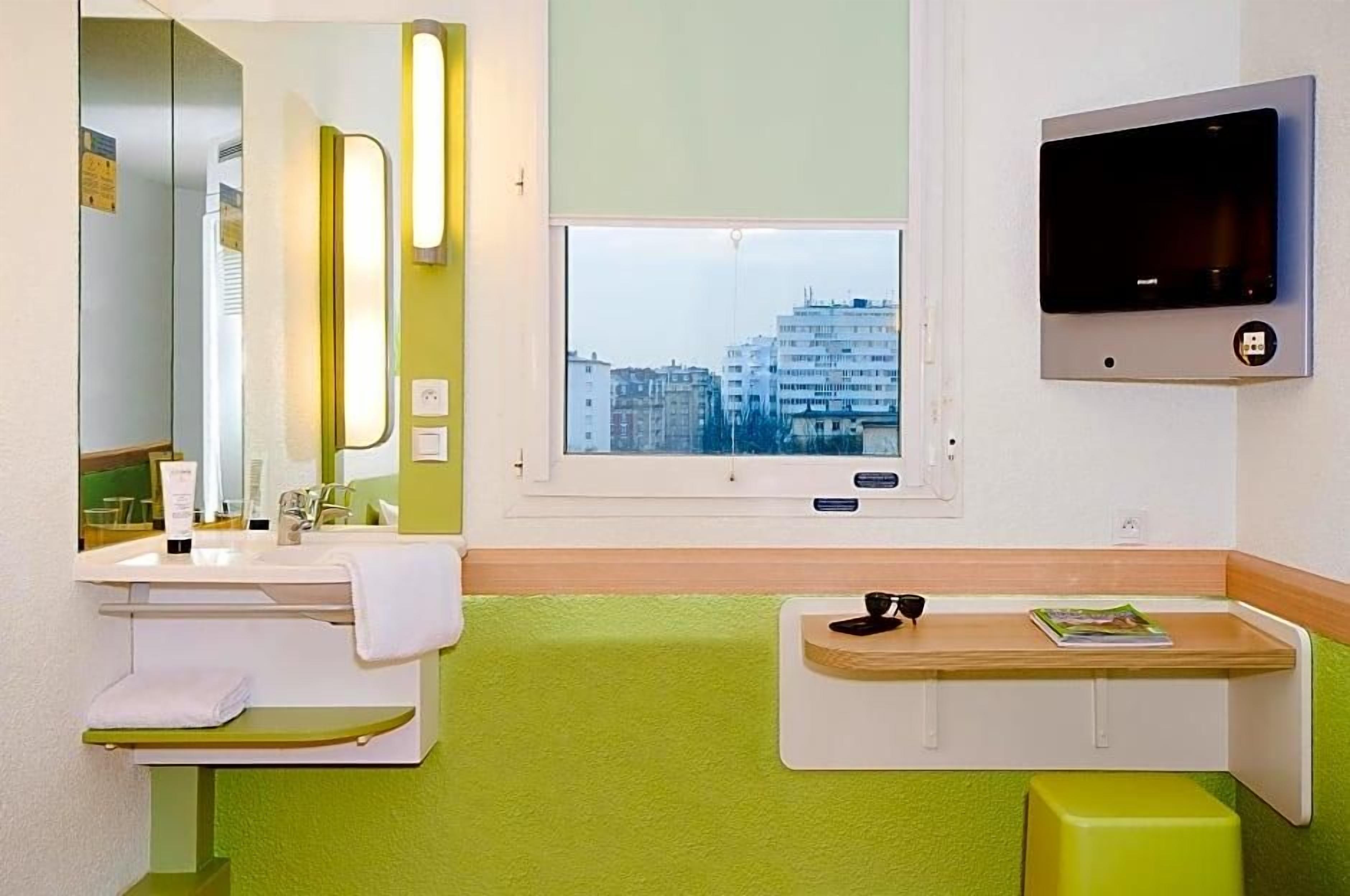 Een badkamer met een wastafel, spiegel, raam en een aan de muur bevestigde televisie.