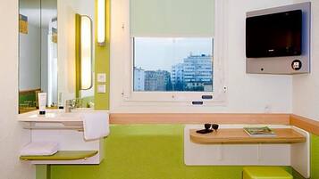 Een badkamer met een wastafel, spiegel, raam en een aan de muur bevestigde televisie.