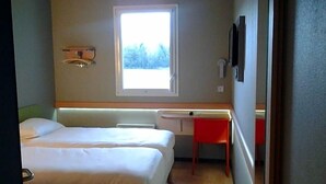 Une chambre avec deux lits, un bureau, une fenêtre et un téléviseur fixé au mur.