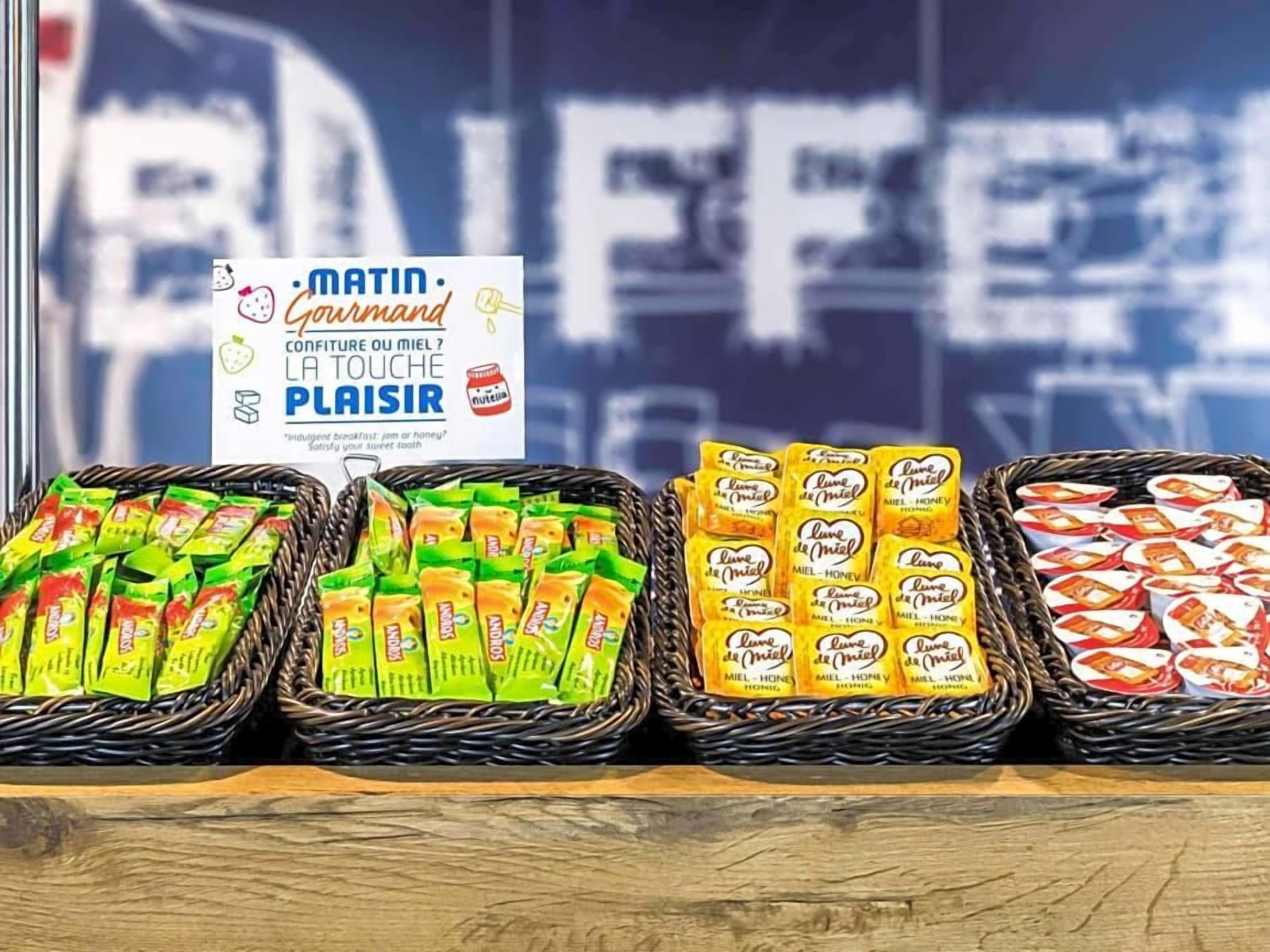Exhibición de alimentos envasados en cestas, un cartel con texto y una ventana con fondo desenfocado.