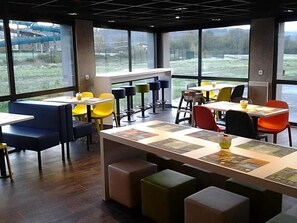A modern dining area with booths and tables, large windows, and a view of the outdoors. - Ibis Budget Givet (Givet)