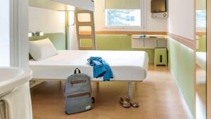 Une petite chambre comprenant un lit superposé, un bureau avec une chaise, une petite fenêtre et un téléviseur.