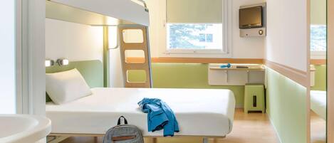 A compact room with a bunk bed, a desk with a chair, a small window, and a TV.