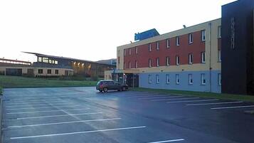 Un parking avec des places délimitées, un bâtiment doté de nombreuses fenêtres et une voiture garée sur le parking.