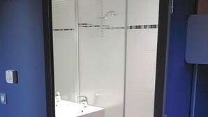A modern bathroom with a glass shower enclosure, a white sink, and a towel rack. - Ibis Budget Givet (Givet)