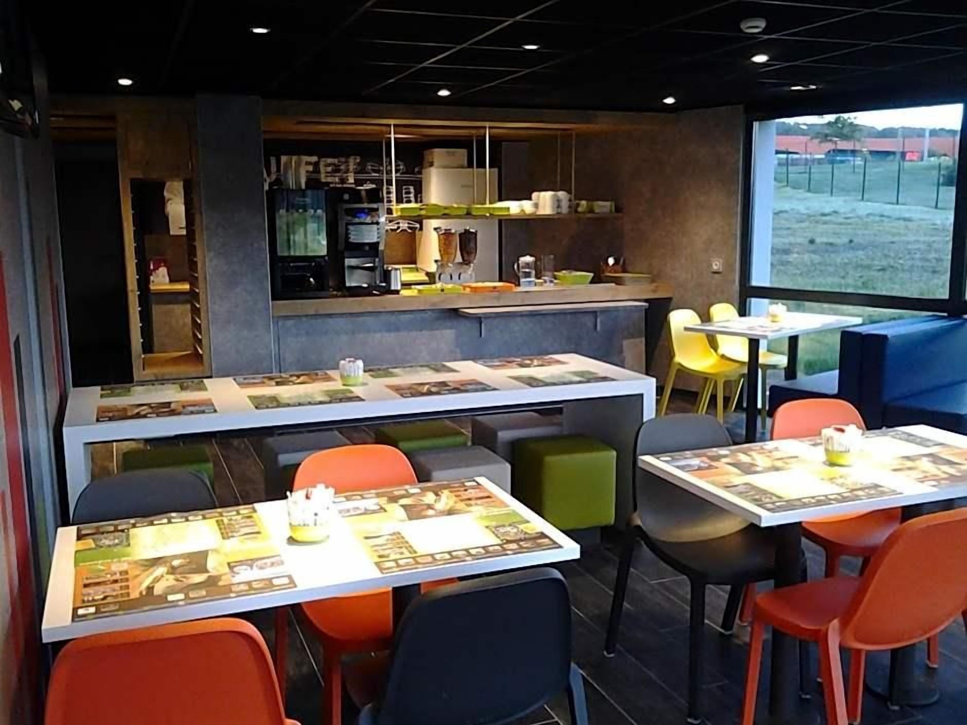 Een restaurant met tafels, stoelen, een toonbank en uitzicht op buiten.