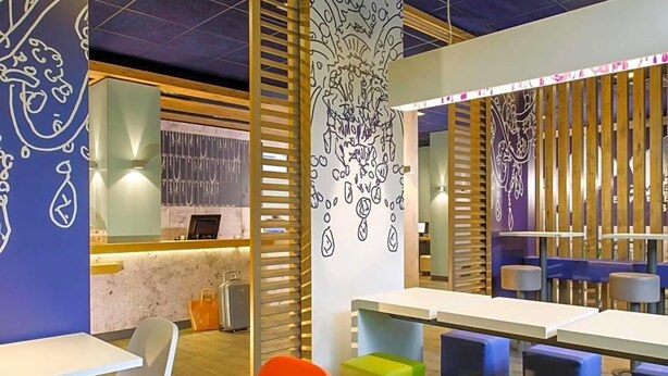 Un intérieur moderne avec des tables et des sièges aux couleurs vives, un comptoir avec un présentoir et des œuvres d’art décoratives sur les murs.