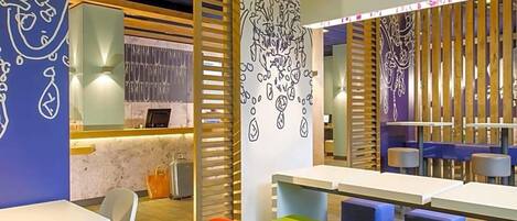 A modern interior with tables and colorful seating, a counter with a display, and decorative wall art.