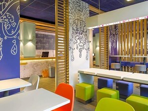 Ein modernes Interieur mit Tischen und farbenfroher Sitzgelegenheiten, einer Theke mit Präsentation und Wanddekoration.