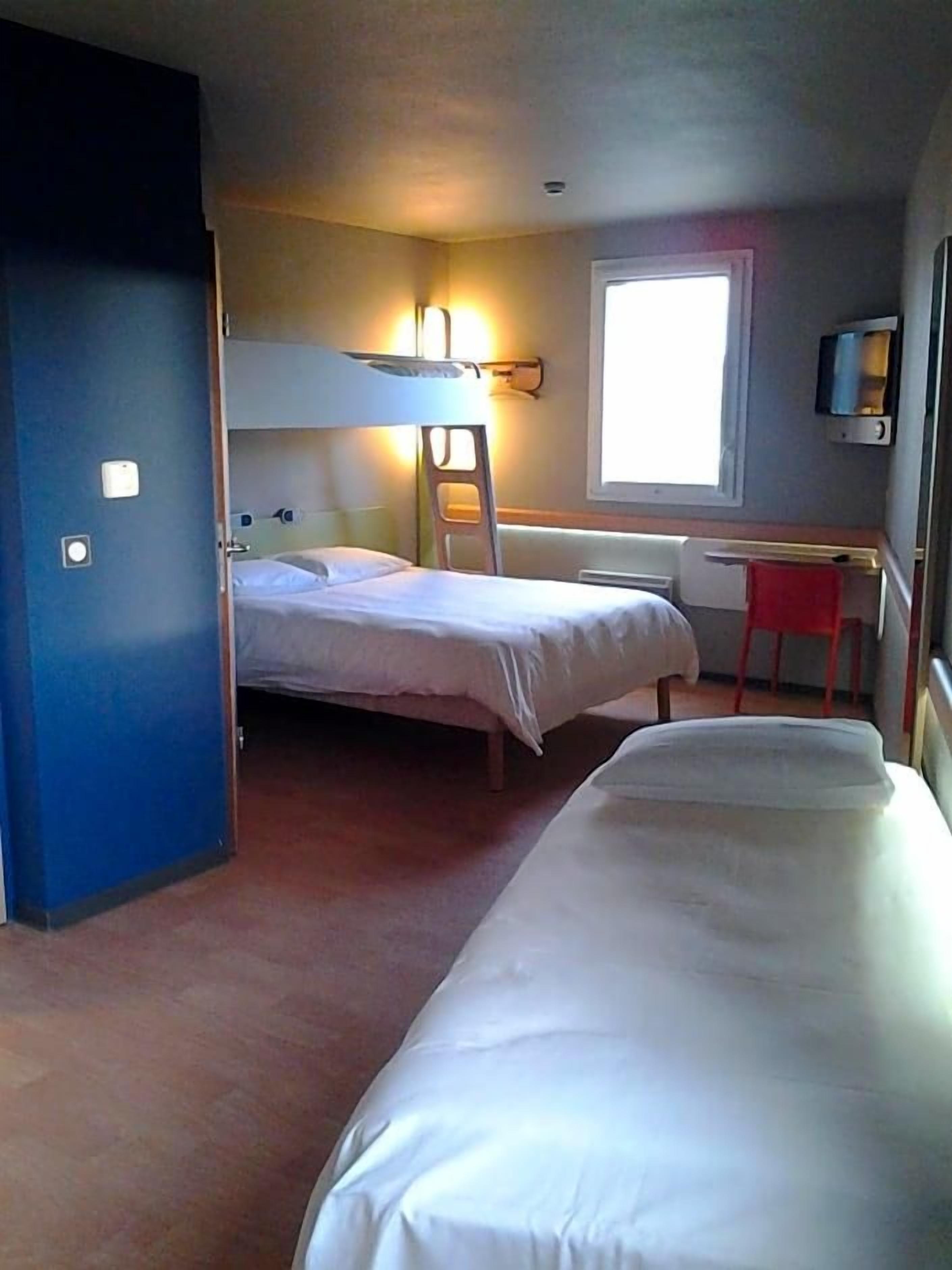 Een kamer met twee bedden, een bureau, een stoel, een raam en een deur.
