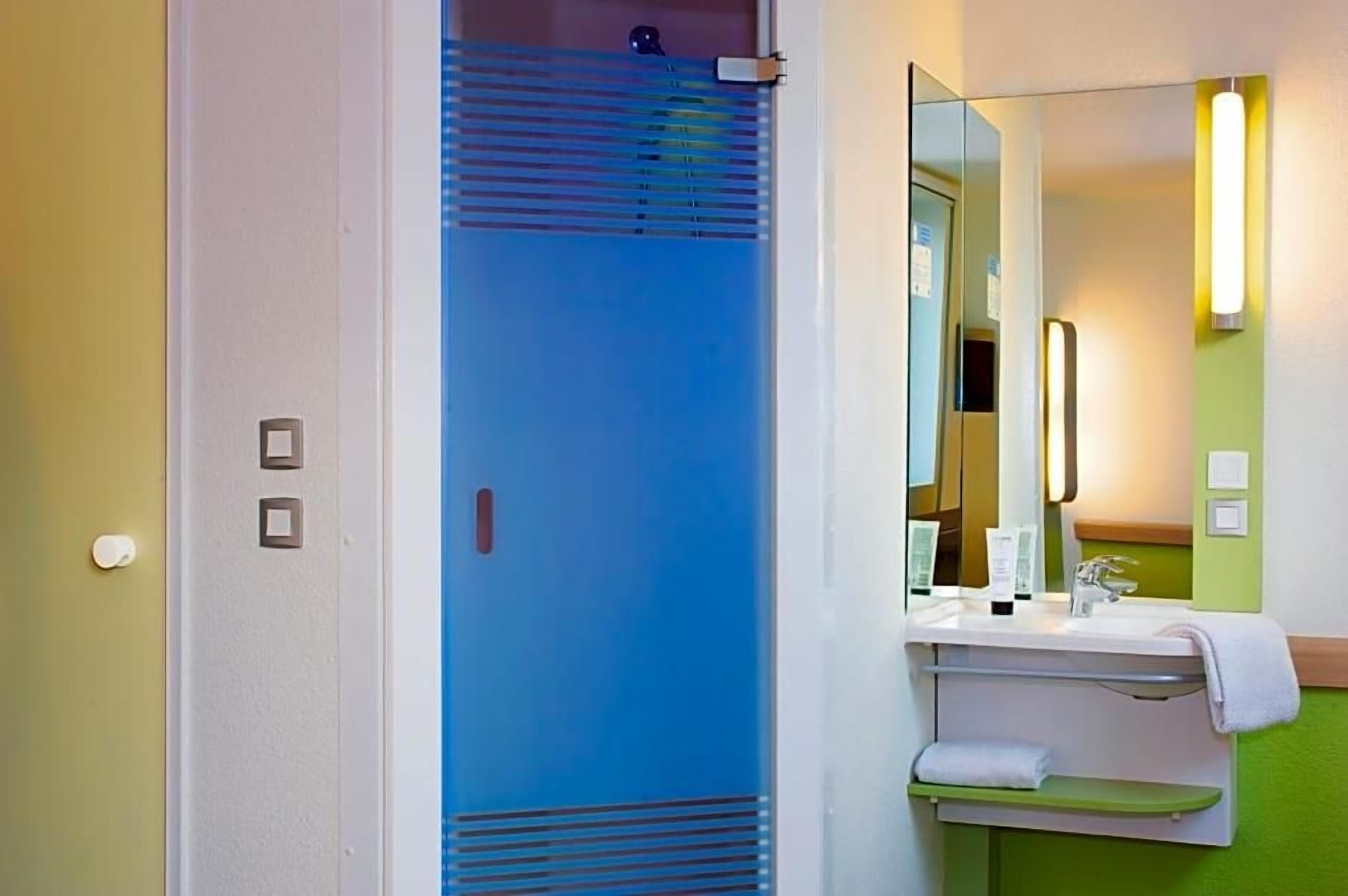 Een badkamer met een blauwe douchecabine, een wastafel met spiegel en een handdoekrek.