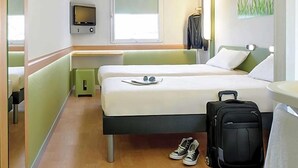 Une chambre d’hôtel avec un lit, une télévision, une fenêtre, un bureau et une valise.