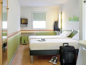 Ein Hotelzimmer mit Bett, Fernseher, Fenster, Schreibtisch und Koffer.