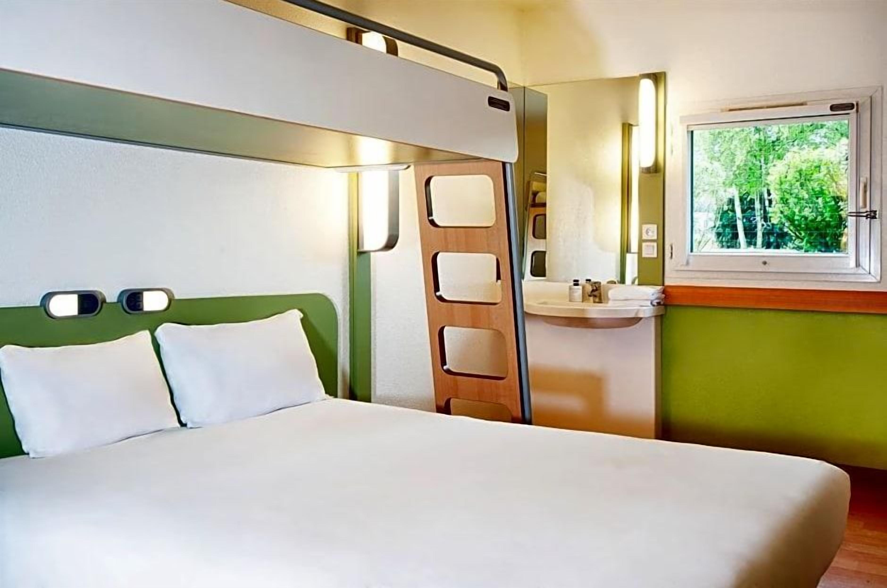 Een kamer met een bed, een raam met uitzicht op bomen, een wastafel en een spiegel.