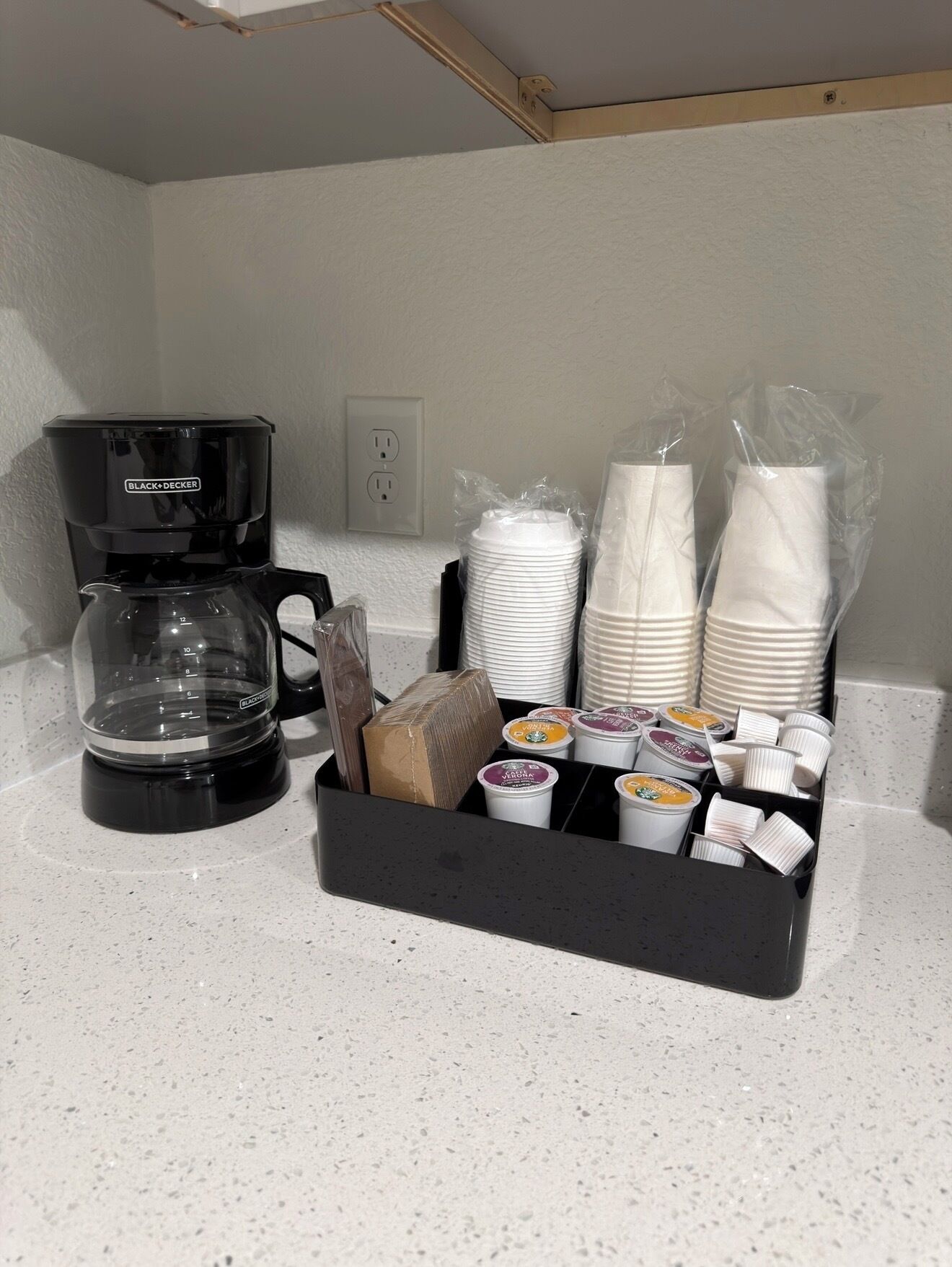 A coffee maker, stacked plates, and a tray of coffee cups on a countertop.