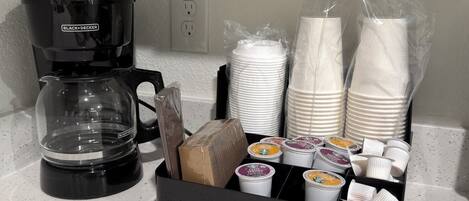 A coffee maker, stacked plates, and a tray of coffee cups on a countertop.