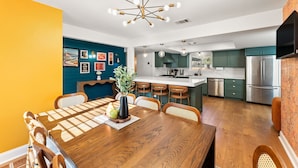 Eine moderne Küche mit Edelstahlgeräten, ein Essbereich mit Holztisch und -stühlen sowie eine Wand in Türkis.