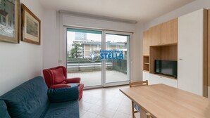 Un appartement moderne comprenant un canapé, une table à manger, un téléviseur et une porte-fenêtre coulissante donnant sur un balcon.