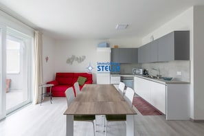 Un soggiorno moderno con zona pranzo, cucina e un divano rosso.