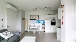 Una sala de estar moderna con un sofá, una mesa de comedor y una cocina con armarios blancos.