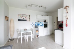 A modern kitchen with white cabinets, a dining area with a table and chairs, and a ceiling light fixture. - Laguna °central area+pool° (Lido di Jesolo)