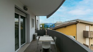 A balcony with a table and chairs, a sliding glass door, and a view of neighboring buildings. - Tiepolo apt. w/beach place + parking (Jesolo)