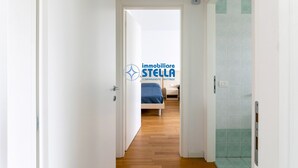 A hallway leading to a bedroom with a bed, a door, and a shower area. - Tiepolo apt. w/beach place + parking (Jesolo)