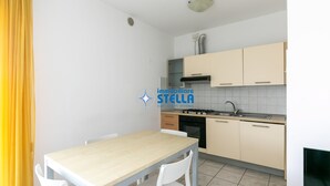 A kitchen with a wooden table and white chairs, beige cabinets, a stove, and a sink. - Tiepolo apt. w/beach place + parking (Jesolo)