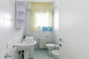 Een badkamer met toilet, wastafel en een raam met gordijn.