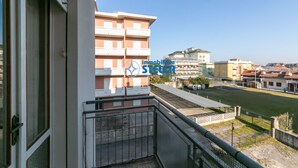 A balcony with a metal railing, a view of a residential area, and a building with a sign that reads 'immobiliare STUDIO'. - Romeo [bilocale+parking] (Lido di Jesolo)