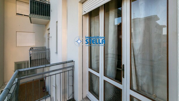 A residential building with a balcony, a sliding glass door, and a window with a curtain. - Romeo [bilocale+parking] (Lido di Jesolo)