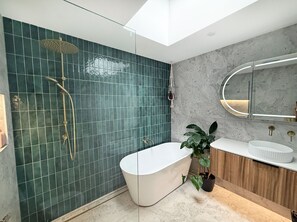 Un baño moderno con una bañera independiente, ducha con cabezal de ducha tipo lluvia, un espejo grande y una planta en maceta.