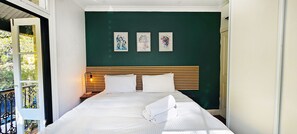 Un dormitorio con cama, mesita de noche, pared verde y tres cuadros enmarcados.