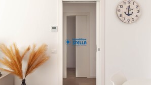 Un pasillo con suelo de madera, una puerta blanca, un reloj de pared y un florero con plumas de pampa.