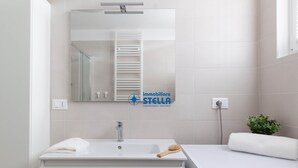 Un baño moderno con lavamanos, espejo, toalla y un calentador de pared.