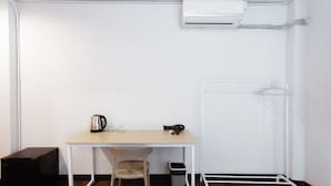 A small room with a wooden desk, a chair, a black storage unit, a white radiator, and a metal drying rack. - Stay On Maya (Chiang Mai)