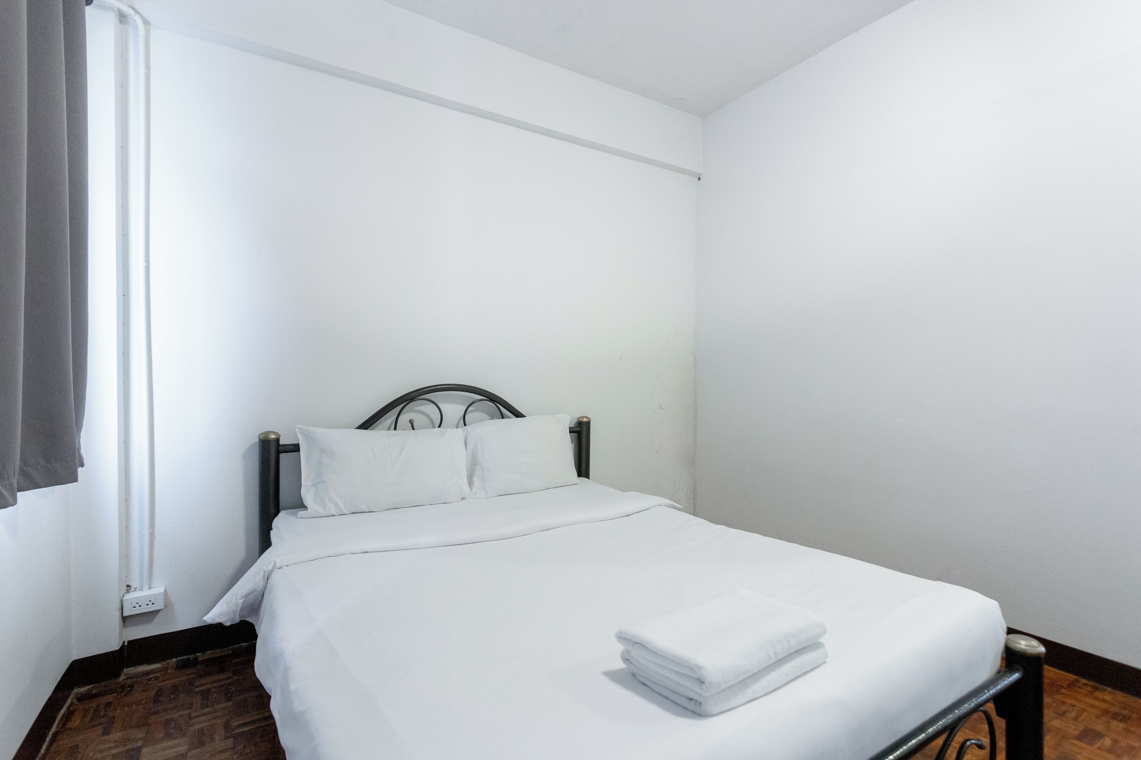 Una cama individual con ropa blanca, cabecera de metal y ventana con cortinas.