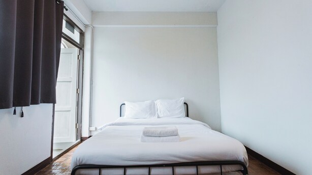 A single bed with white bedding, a bedside table, and a window with curtains. - Stay On Maya (Chiang Mai)