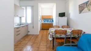 Eine kleine Küche mit weißen Schränken, ein Essbereich mit Tisch und Stühlen sowie ein Fernseher auf einem Schrank.