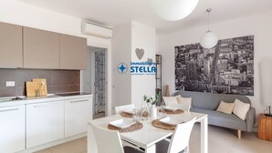 Una cucina moderna con mobili bianchi, un'area pranzo con tavolo bianco e un divano grigio.
