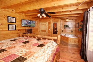Ein Interieur einer Holzhütte mit Bett, Fernseher, Bad und Deckenventilator.